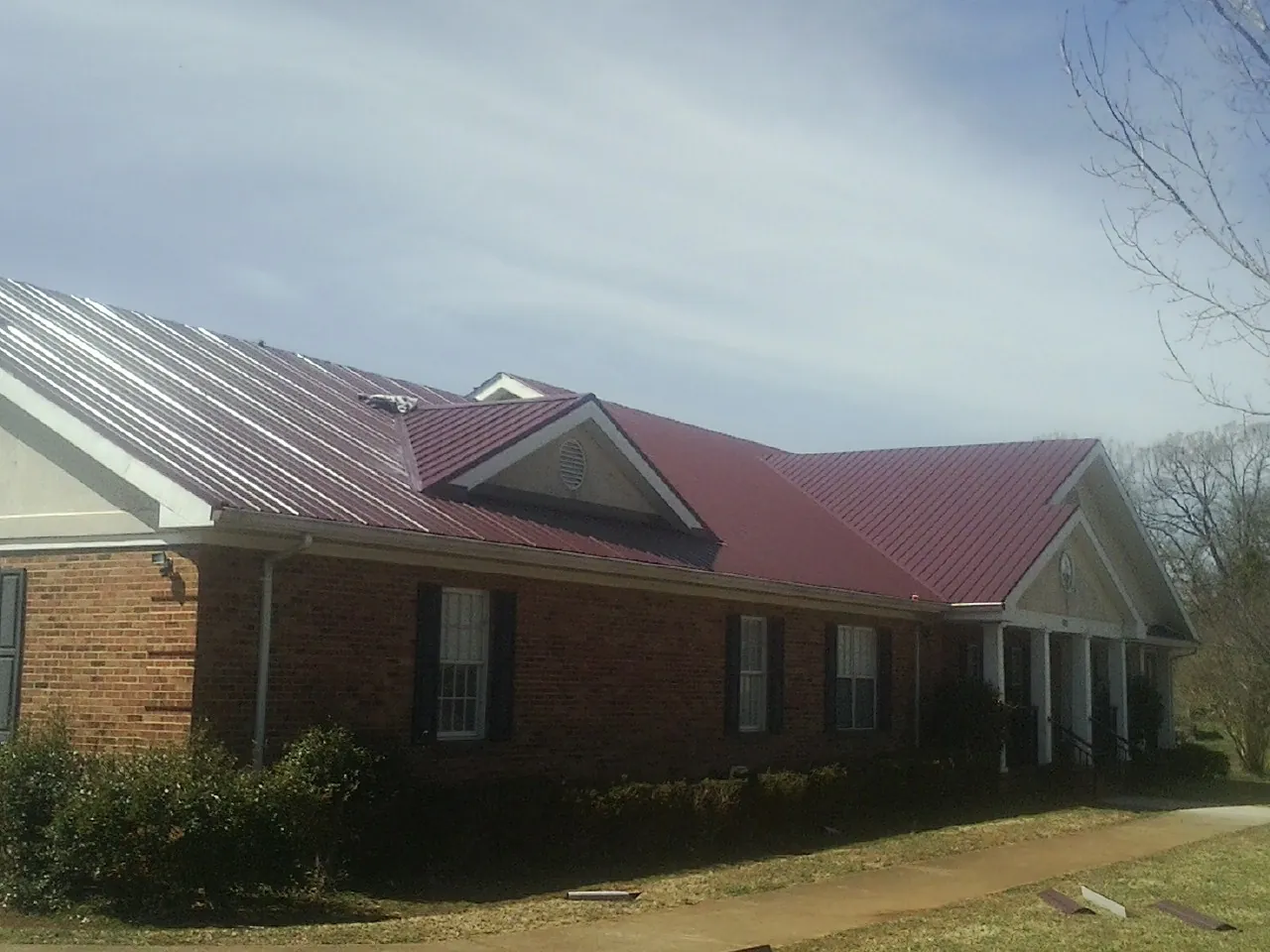 Red metal roof with gabled entries on a long brick building, from a Hail Damage Roof Repair job in Altaville