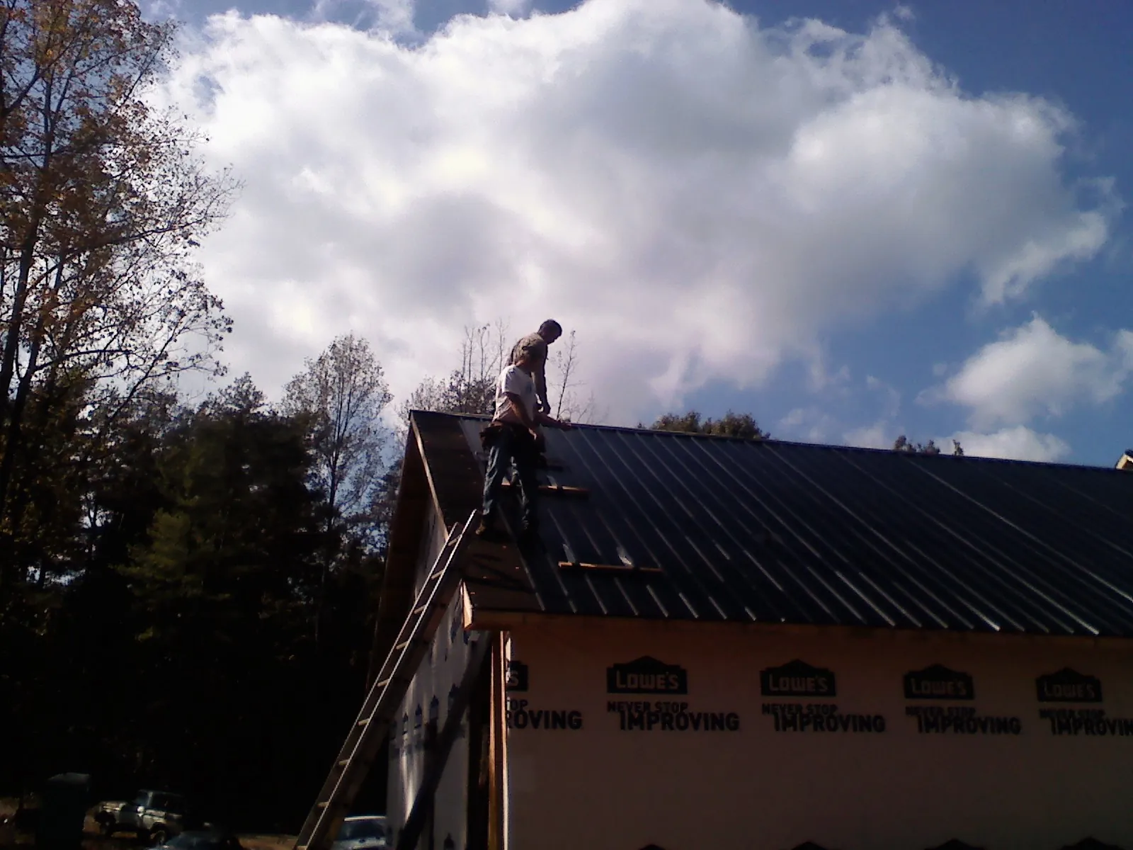 Roofer fastening dark metal panels high against a cloudy sky, from a Roof Inspection job in Altaville