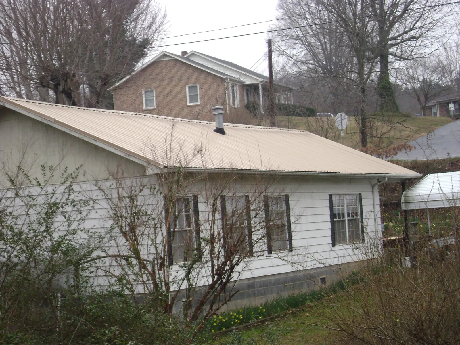 Tan metal roof on a white sided house set into a hillside — Commercial Roofing by Roofing Brothers in Altaville